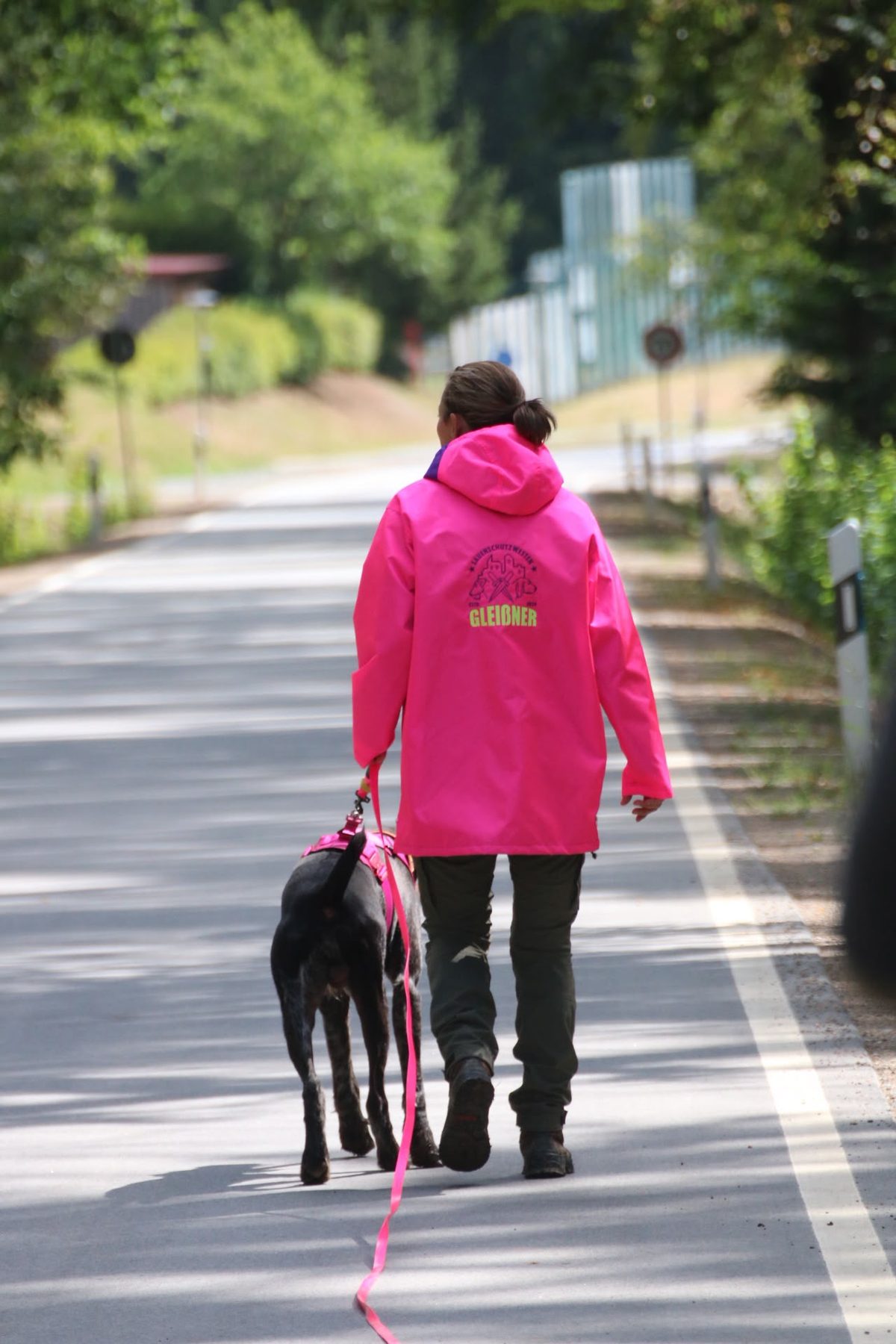 Hundeführerin mit pinker Gleißner-Hundeführerjacke und Hund an der Leine, Rückansicht